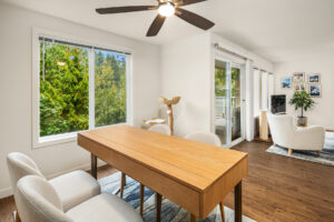 Modern apartment dining area with wood floors, large windows showcasing lush greenery, and balcony access at Wildwood Apartment Homes in Issaquah, Washington.