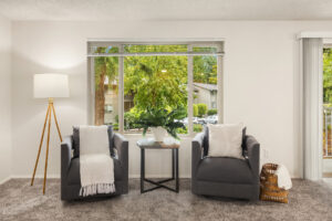 Apartment seating area with two gray chairs, carpet flooring, and large window overlooking trees at Wildwood Apartment Homes in Issaquah, Washington.