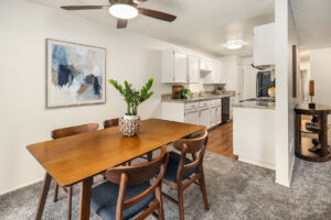 Apartment dining space with wood table, carpet flooring, ceiling fan, and view of updated kitchen at Wildwood Apartment Homes in Issaquah, Washington.